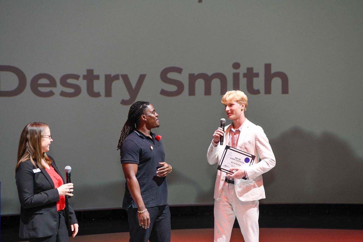 Two people smiling while a third speaks into a microphone